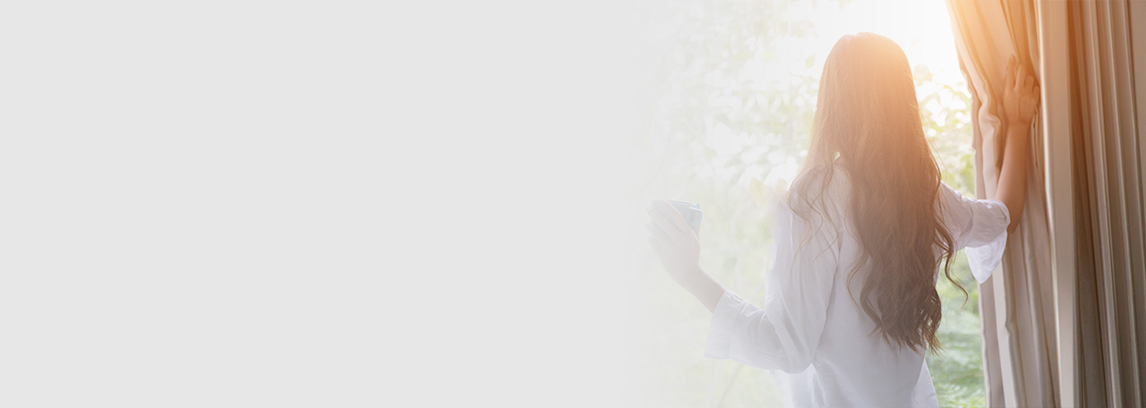 Женщина смотрит на улицу, отодвинув шторы.
